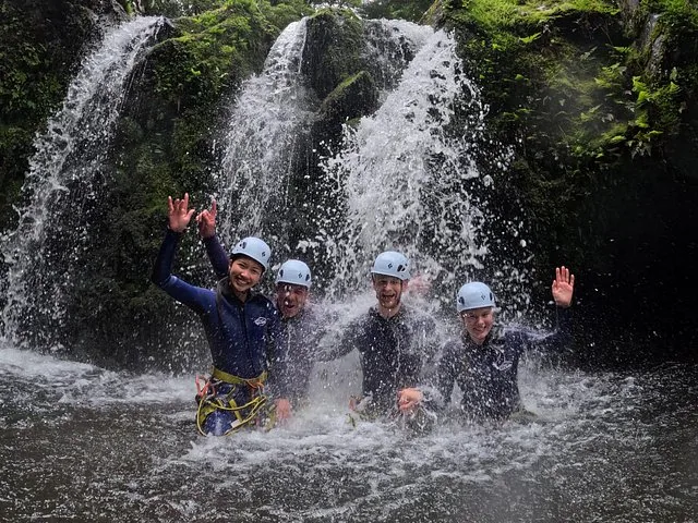 Group of four people in wetsuits smiling under a waterfall in Ribeira dos Caldeirões