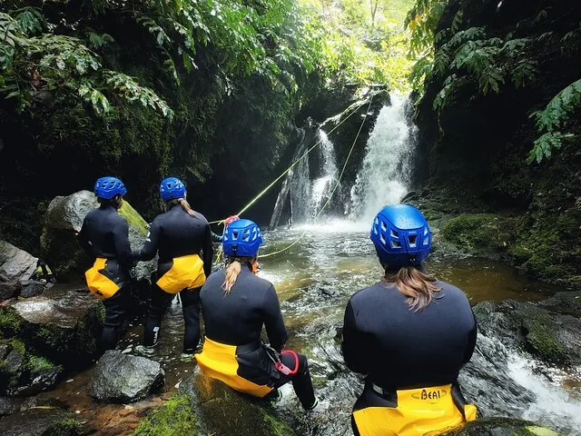 Gruppe von Menschen in Neoprenanzügen, die sich darauf vorbereiten, einen Wasserfall abzuseilen