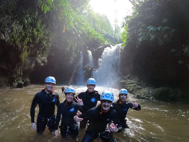 Gruppe von fünf Personen in Neoprenanzügen, die lächelnd in einem flachen Fluss stehen