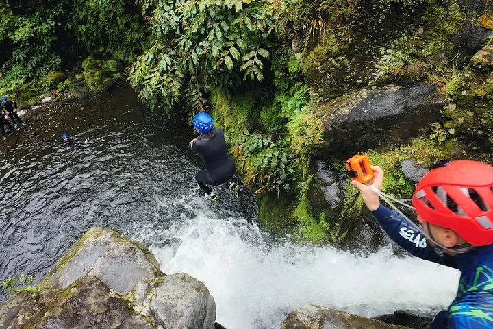 Person in a wetsuit jumping into a pool at the bottom of a waterfall