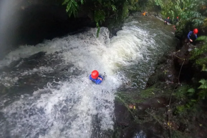 Person im Neoprenanzug und mit rotem Helm, die einen schnell fließenden Wasserfall hinunterrutscht